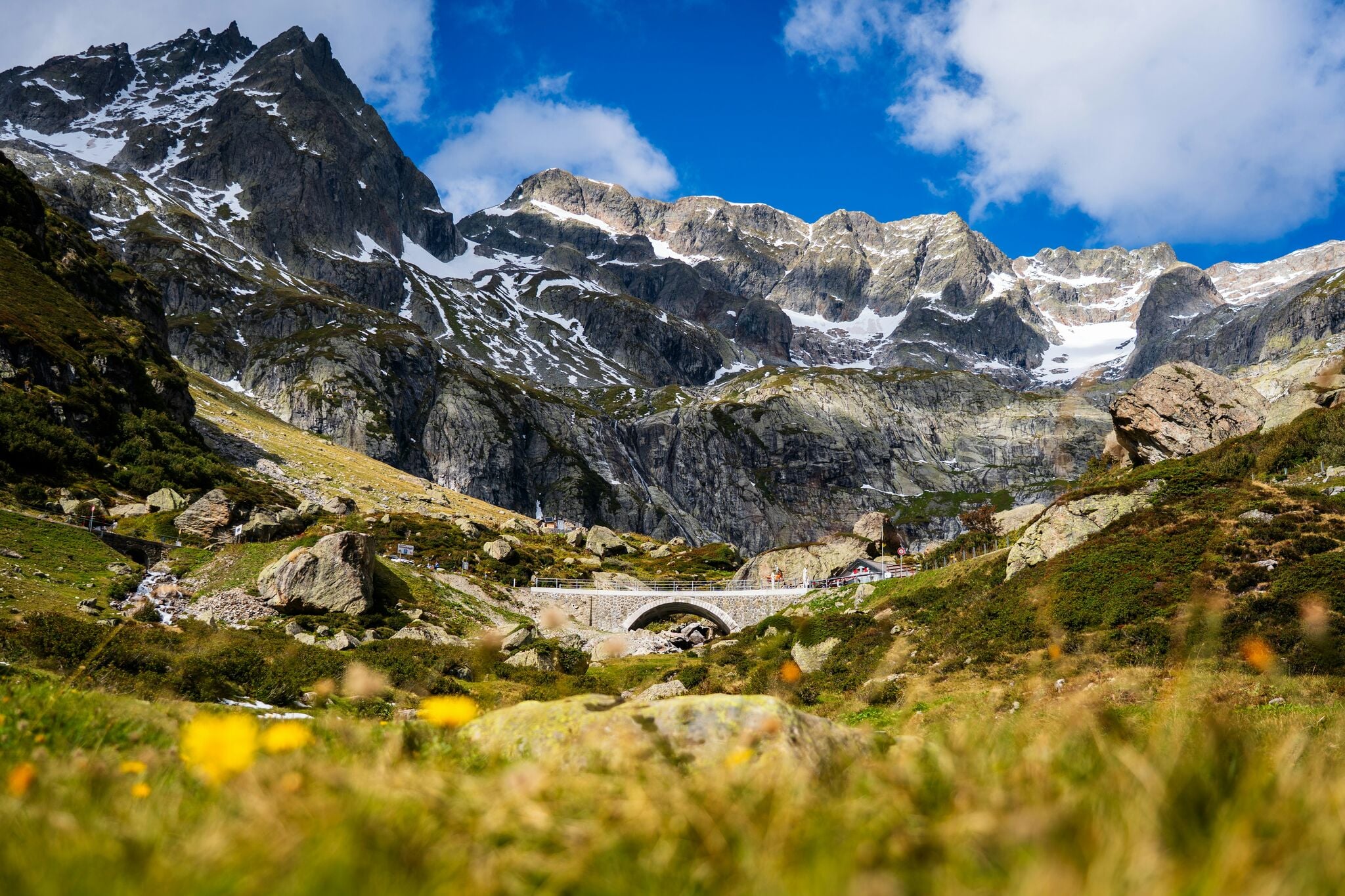 Bergbrücke in schneebedeckter Alpenlandschaft mit Haus, Kombination aus Natur und Architektur mit malerischen Felsen und Vegetation bei Tageslicht.